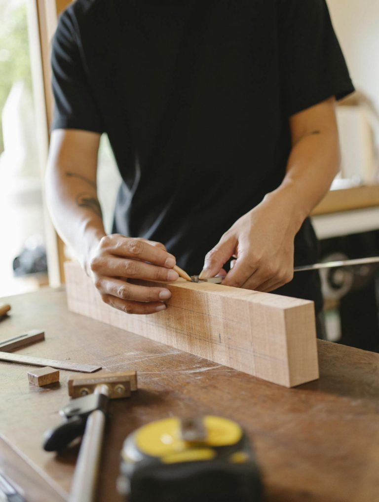 Crop unrecognizable male joiner making sign on wooden plank with pencil while making handicraft in workshop